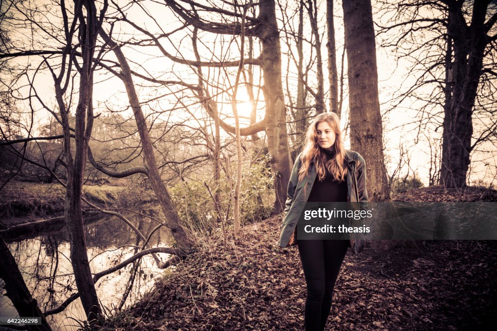 Beautiful young woman in black walking by a river