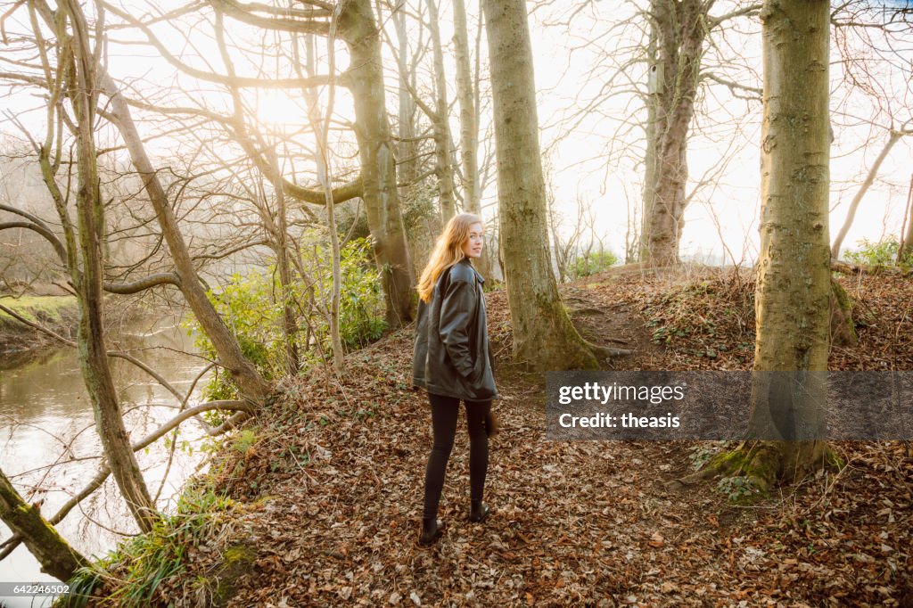 Beautiful young woman in black walking by a river