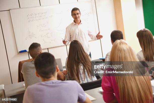 smiling teacher giving lecture to students in classroom. - high school maths stock pictures, royalty-free photos & images