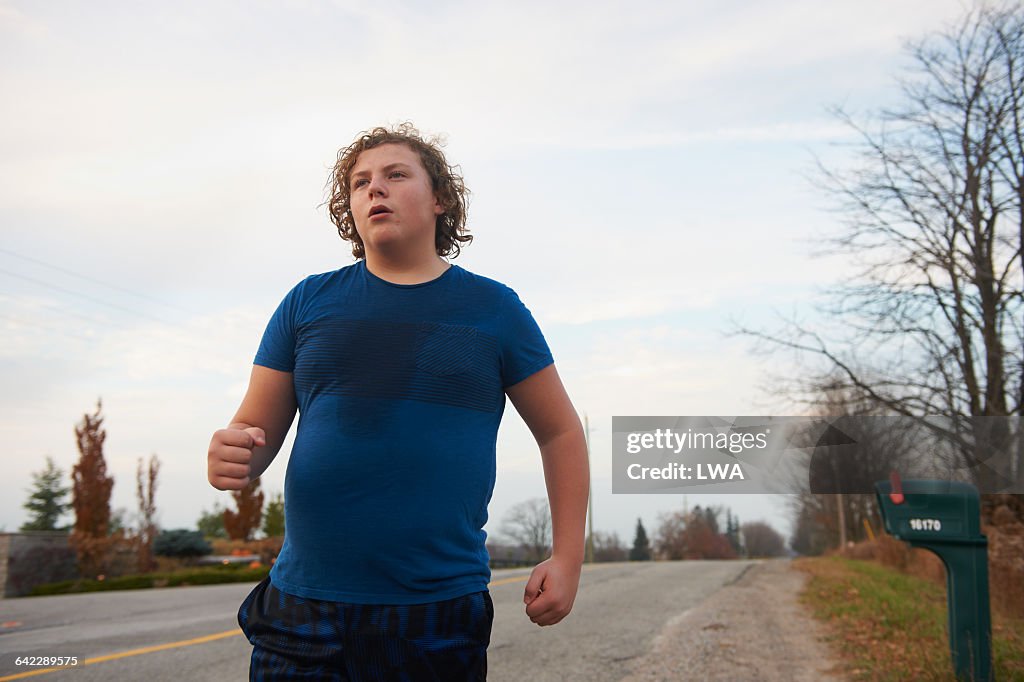 Teen boy jogging on country road