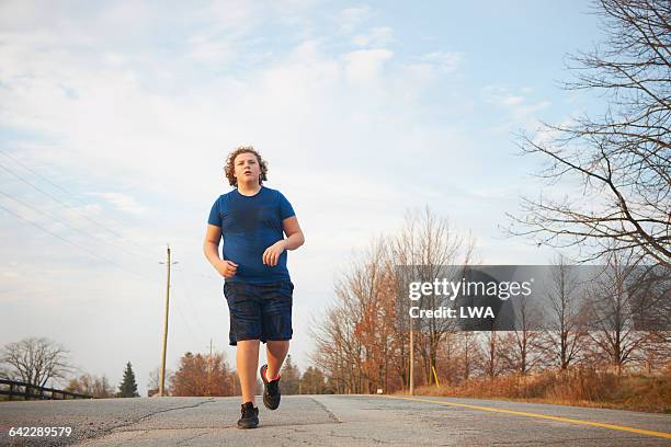 teen boy jogging on country road - teen boy shorts stock-fotos und bilder