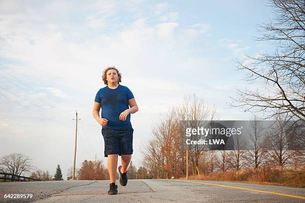 teen boy jogging on country road - chubby teenager photos et images de collection