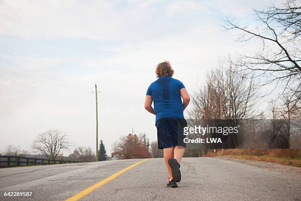 teen boy jogging on country road - teen boy shorts stockfoto's en -beelden