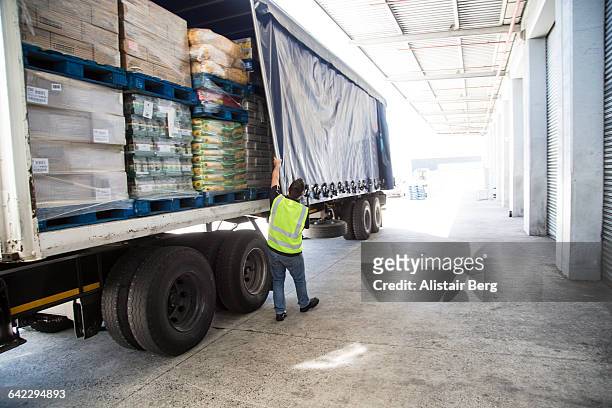worker loading a lorry at a large warehouse - tarpaulin fotografías e imágenes de stock