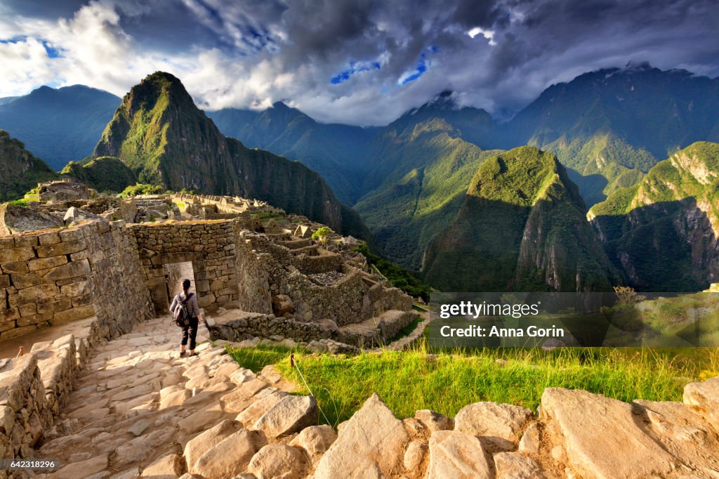 Back view of female tourist descending stairs overlooking Machu Picchu ruins at sunset, Peru