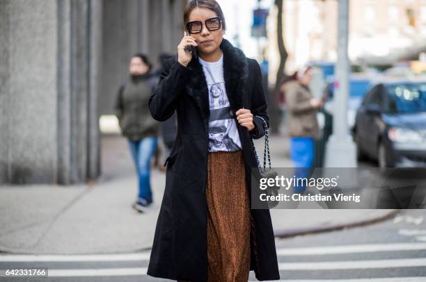 Guest wearing a blackk coat, tshit with print outside Marc Jacobs on February 16, 2017 in New York City.