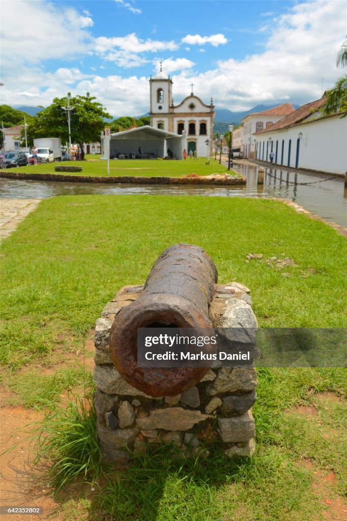 Rusted ancient defensive cannon and Capela de Santa Rita in Paraty, Rio de Janeiro