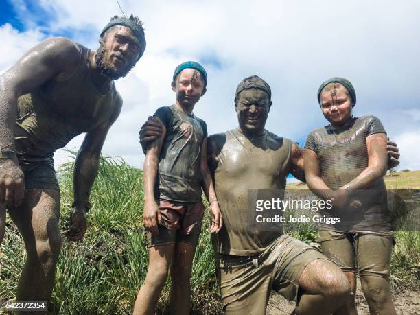 Group of adults and children standing together covered in mud during a mud run event