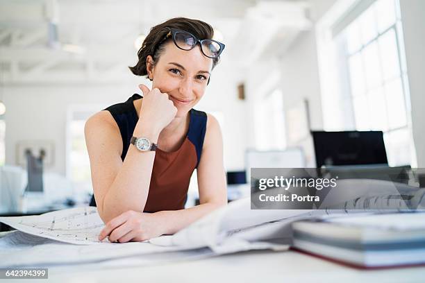 smiling woman with blueprints in office - architects stock-fotos und bilder