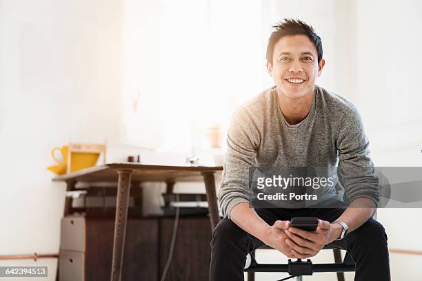 happy businessman holding phone in office - asian man sitting casual imagens e fotografias de stock