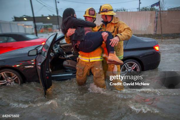 Firefighter carries a woman from her car after it was caught in street flooding as a powerful storm moves across Southern California on February 17,...