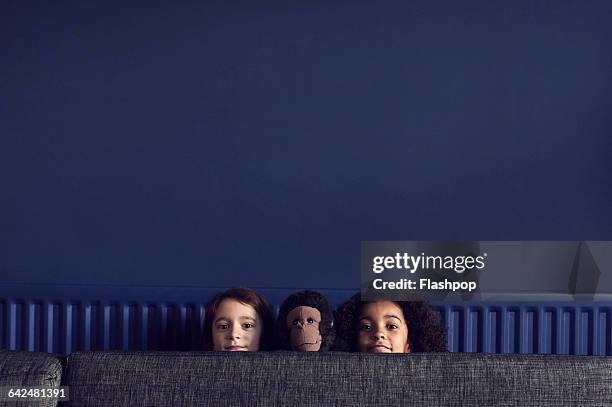 two girls and toy monkey peering over sofa - navy blue living room stock pictures, royalty-free photos & images