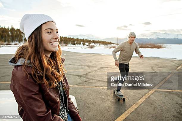 young woman and man with skateboard at sunset - winter hat stock pictures, royalty-free photos & images