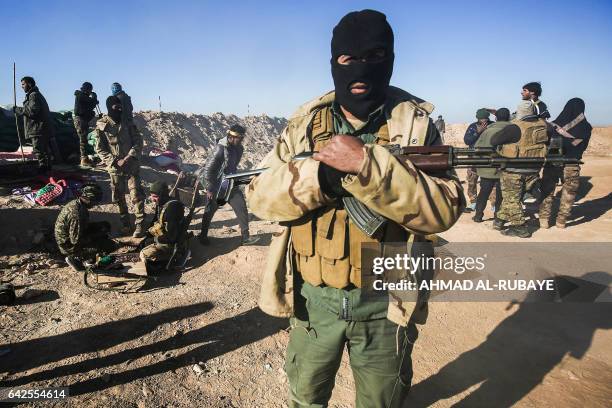 Masked fighter of the Hashed al-Shaabi paramilitaries poses for a picture carrying a Kalashnikov assault rifle by defensive positions near the...