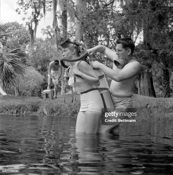 Preparing for a "lab" session, teacher Bruce Mozert, helps Ginger into an aqualung so she can breathe underwater. On the bank, Bill Ray pumps air...
