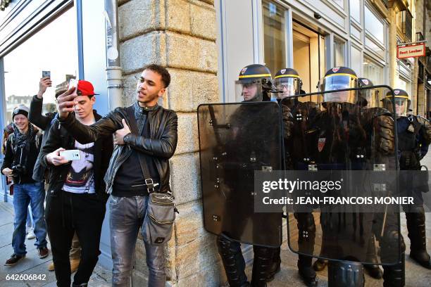 Young men take provocative selfie photos as anti-riot police officers stand guard during a demonstration against police brutality on February 18,...