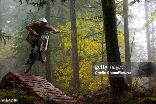 a man jumps off a wooden bridge on his downhill mountain bike on a foggy day in british columbia, canada. - bicycle stunt stock pictures, royalty-free photos & images