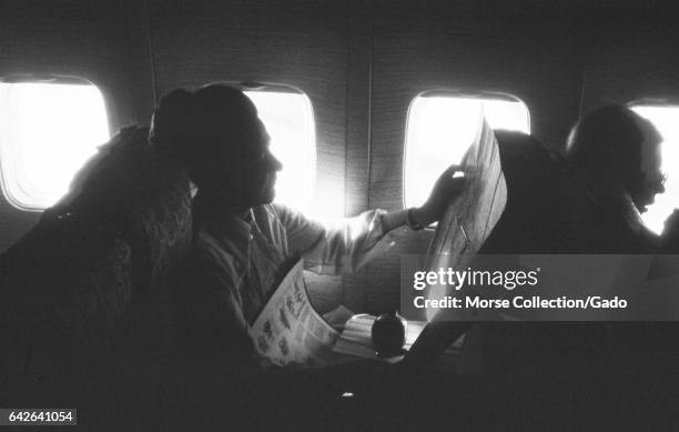 View of a woman reading a newspaper at her window seat on a Turkish Airlines flight, in Istanbul, Turkey, November, 1973. .