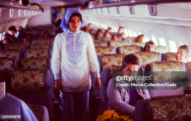 Interior view of a Turkish Airlines airplane, in Istanbul, Turkey, November, 1973. Travelers are seated throughout the plane, and a woman poses in...