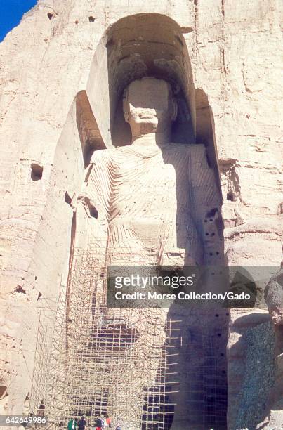 View of the taller Bamiyan Buddha statue, known as Salsal, standing in his giant niche, November, 1975. A group of tourists standing at the base are...