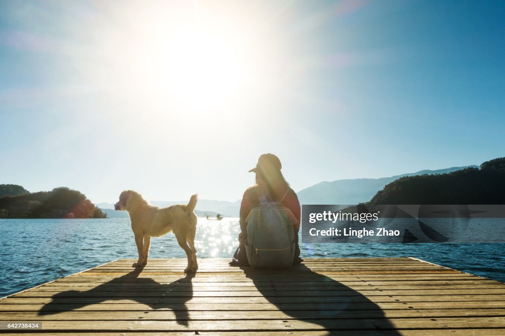 Young woman sitting by pier with dog