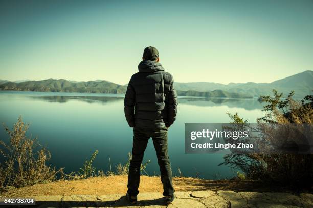 young man standing by lake - breitbeinig stehen stock-fotos und bilder