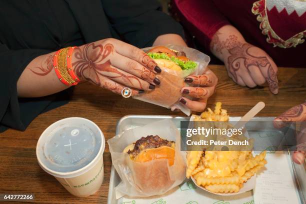 Women from Bahrain, with henna tattoos on their hands, tuck into a Shake Shack burger and chips at the Mall of the Emirates, a premier shopping mall...