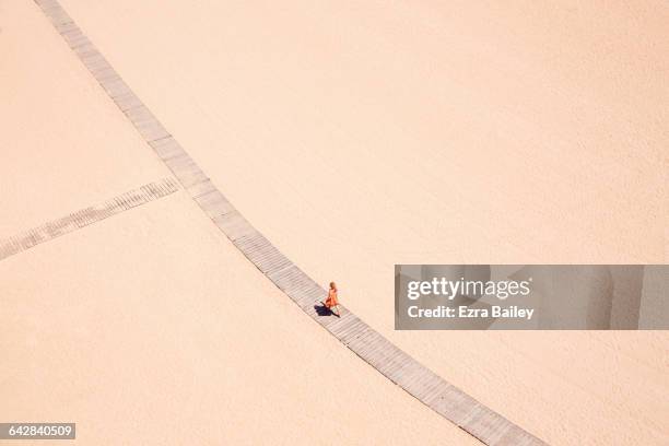 Woman in orange walks along beach boardwalk