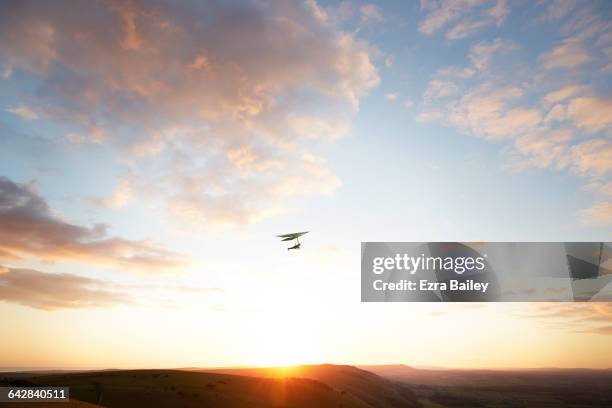 hang glider flying over hills at sunset - drachenfliegen stock-fotos und bilder