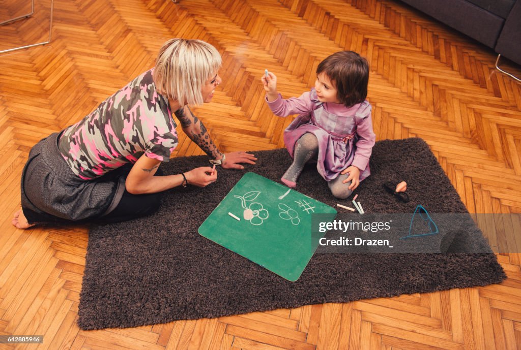 Mother and her daughter chalk drawing on blackboard at home, having joy and unforgettable moments