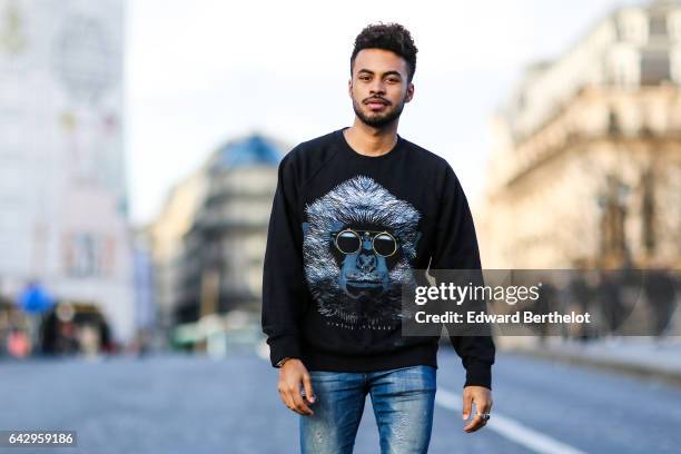 Theo Kimbaloula, fashion blogger, wears a Zwitter pull over with a printed logo representing a monkey with sunglasses, Asos blue denim jeans pants,...