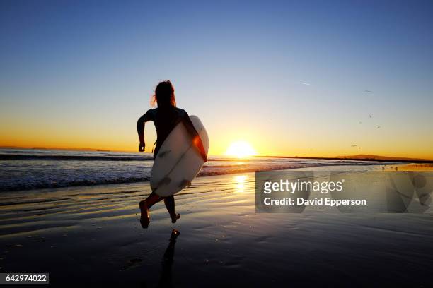 woman running on beach with surfboard at sunset - seal beach stock pictures, royalty-free photos & images