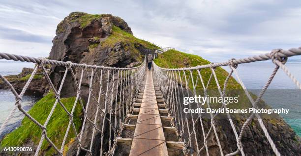 a man crossing the carrick-a-rede rope bridge in antrim, northern ireland - giants causeway stock-fotos und bilder