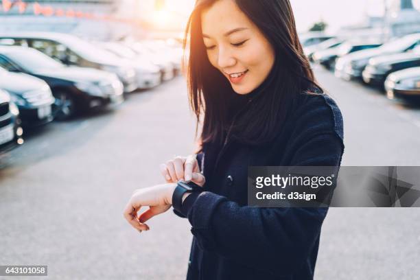 smiling young asian girl checking her smart watch in city street - watch timepiece photos et images de collection