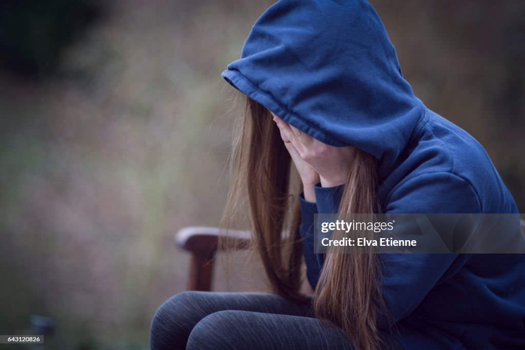 Teenage girl in hooded top, with head in hands in despair