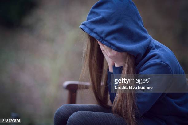 teenage girl in hooded top, with head in hands in despair - childhood stock pictures, royalty-free photos & images