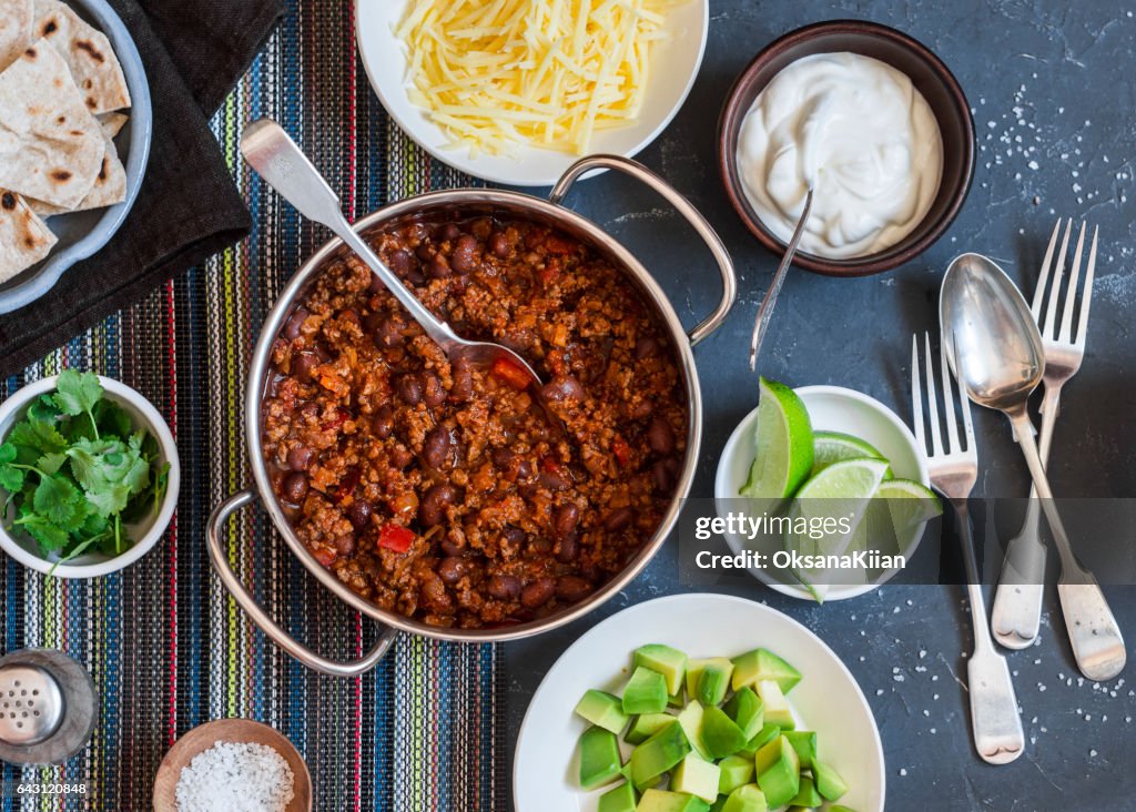 Beef and black bean chili bar on dark background, top view. Flat lay