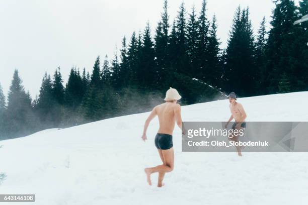 Amigos correndo na neve após a lavagem na banheira de hidromassagem ao ar livre
