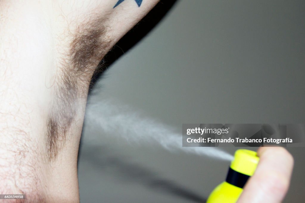 Man applying deodorant spray on the armpit