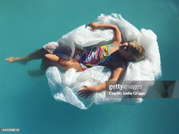 child using a pile of discarded bubble pack as an inflatable pool lounge - luftpolsterfolie stock-fotos und bilder