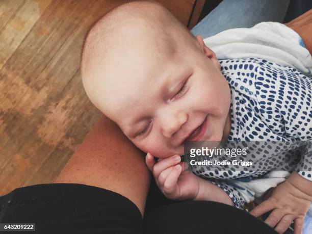 young infant smiling in sleep while being held in mothers arms - baby eltern von oben stock-fotos und bilder