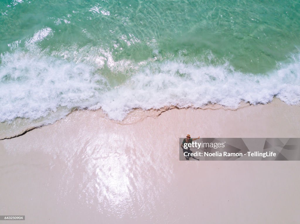 Aerial view of Hyams Beach with one woman at the shore waving at the camera, Jervis Bay, Australia