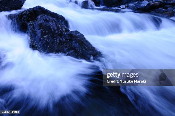 river flow and a black luster rock splitting the water - 急流 stock pictures, royalty-free photos & images