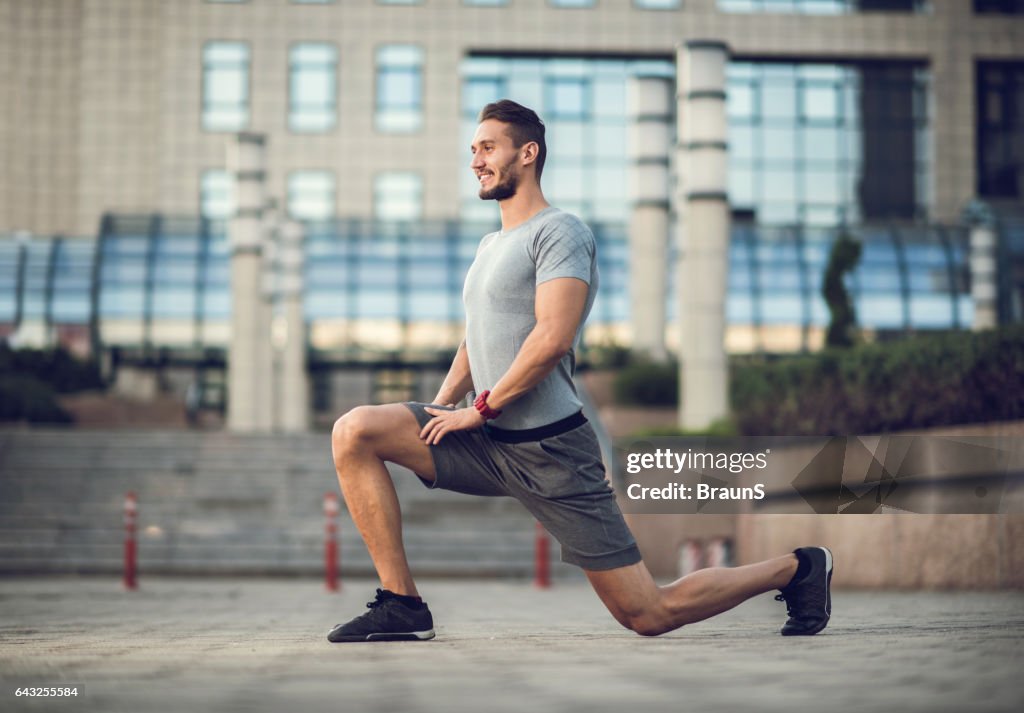 Happy male athlete exercising lunges on the city street.