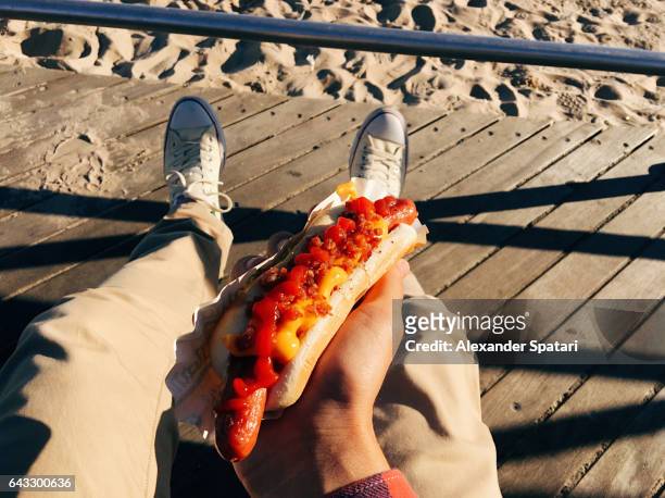 eating famous new york hot dog at coney island boardwalk, personal perspective - fat guy on beach stockfoto's en -beelden