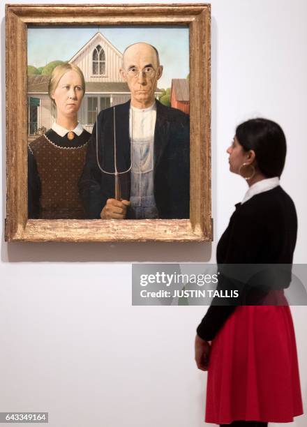 Gallery assistant poses alongside an artwork entitled "American Gothic" by US painter Grant Wood, during a photocall to promote the forthcmoing...