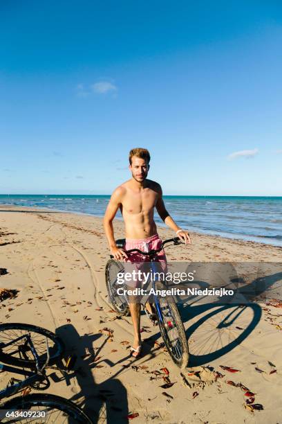 pedaling on the beach - homens jovens stock pictures, royalty-free photos & images