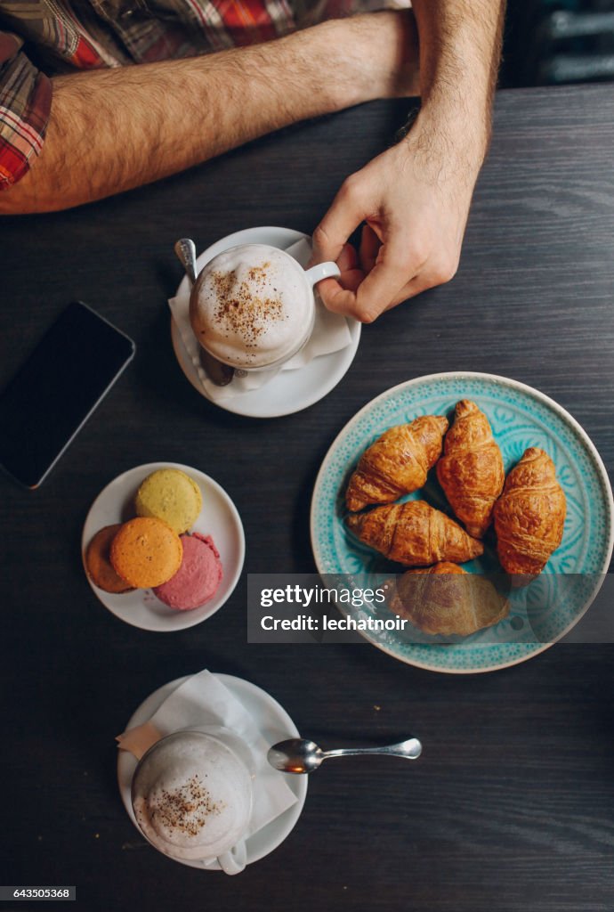 Hombre joven relajándose en la cafetería, con café y medialunas