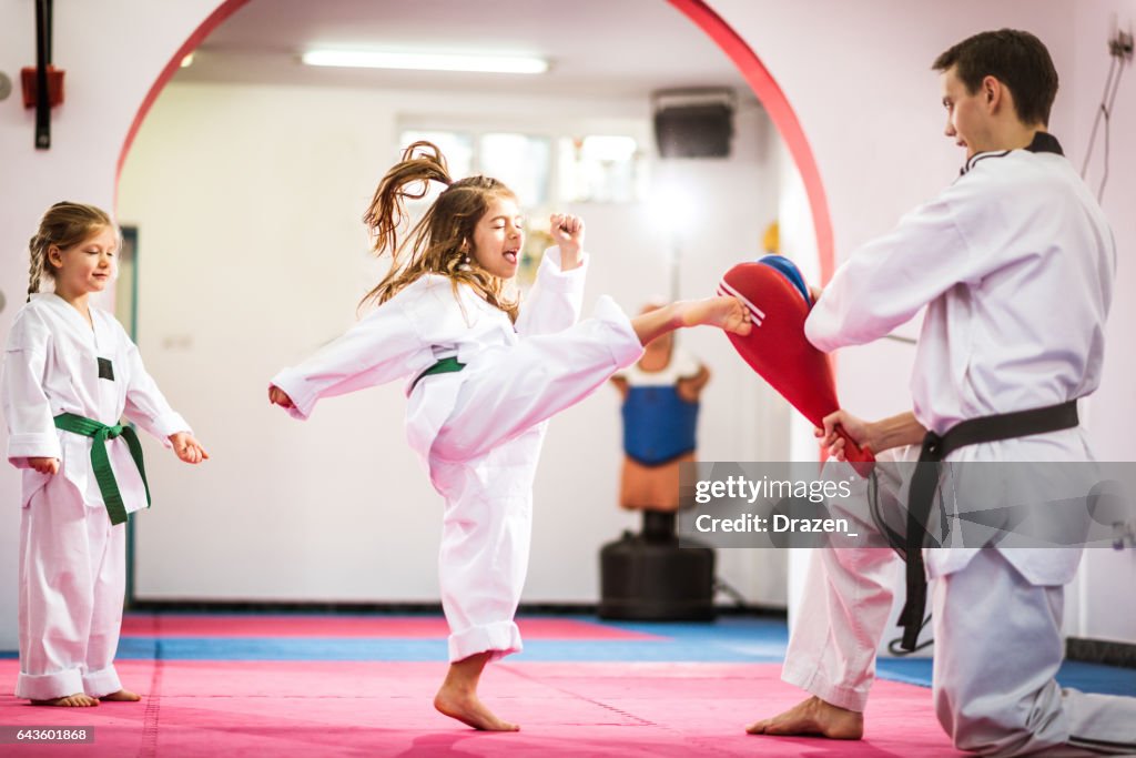 Two cute girls on taekwondo training, kicking and learning self-defence