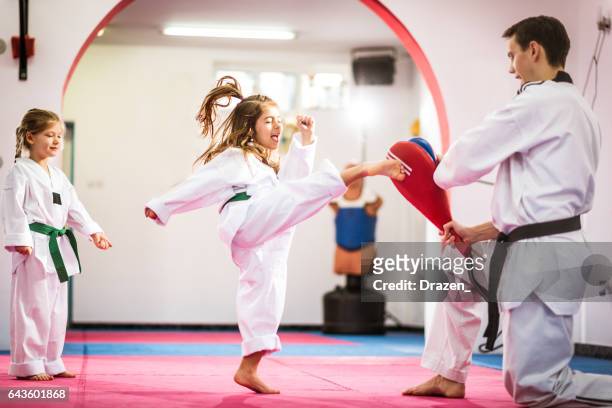 two cute girls on taekwondo training, kicking and learning self-defence - martial arts stock pictures, royalty-free photos & images